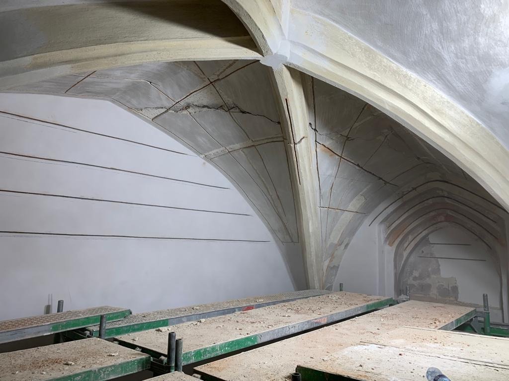 Wnętrze kamienicy z łukowym sklepieniem w trakcie renowacji, widoczne rusztowania i ślady napraw na suficie.