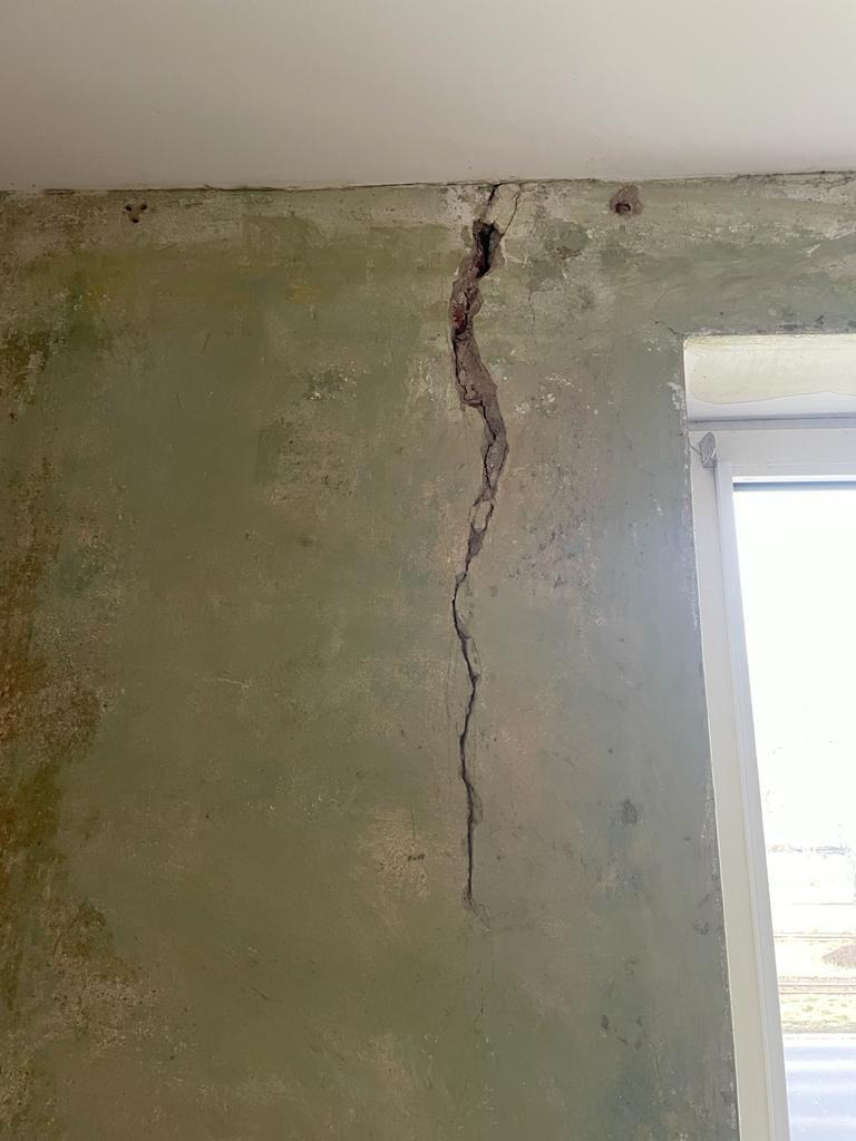 Pęknięcie pionowe ściany wewnętrznej z widocznymi śladami po starych mocowaniach, obok okna.