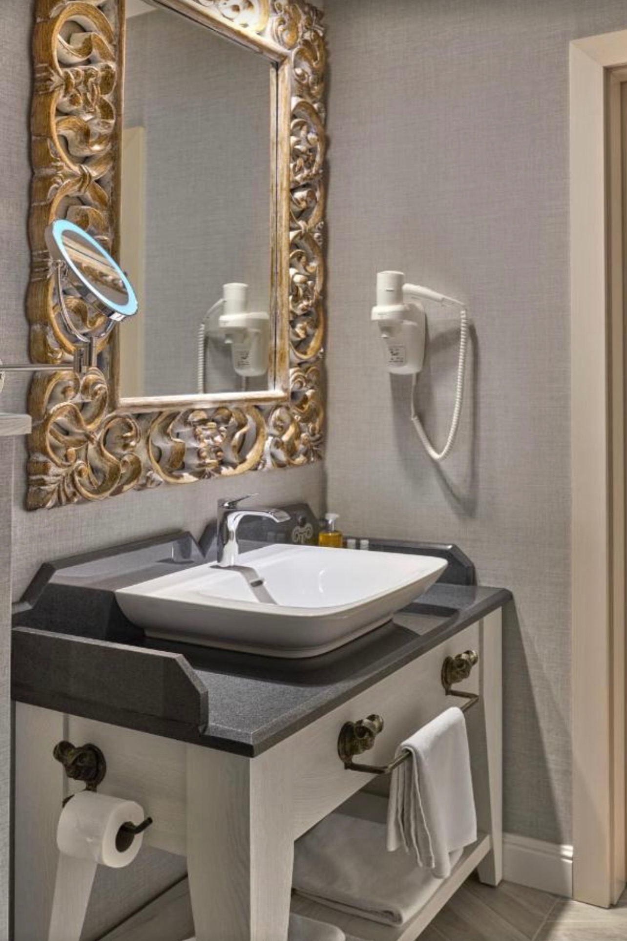 Elegancka łazienka z umywalką nablatową, ozdobnym lustrem w złotej ramie i designerskimi uchwytami na ręczniki w kształcie lwich głów. Nowoczesny styl.