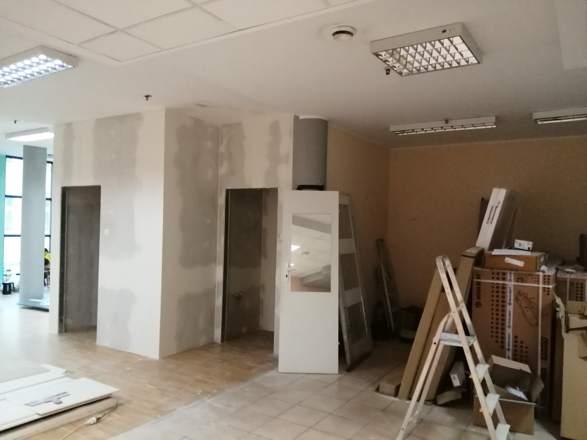 Wnętrze biura w Gorzowie Wielkopolskim w trakcie prac wykończeniowych: szpachlowane ściany, surowe ościeżnice, widoczna drabina i materiały budowlane.