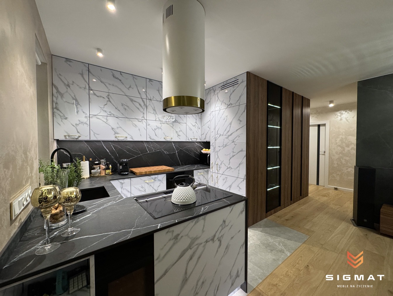 Nowoczesna kuchnia z białymi szafkami górnymi z marmurowym wzorem, czarnym blatem i wyspą z białym marmurowym frontem, uzupełniona o drewnianą zabudowę z przeszklonymi witrynami i złotymi akcentami.