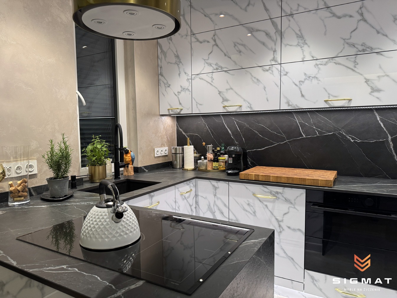 Nowoczesna kuchnia z białymi szafkami górnymi imitującymi marmur, czarnym blatem z marmurowym wzorem, czarną armaturą i białym czajnikiem na płycie indukcyjnej.