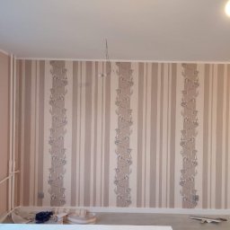 Vladyslav Vashchuk - Pokój po tapetowaniu w pionowe pasy z motywem kwiatowym, widoczne drobne niedociągnięcia przy podłodze, grzejnik, oraz wystające kable od lampy sufitowej.