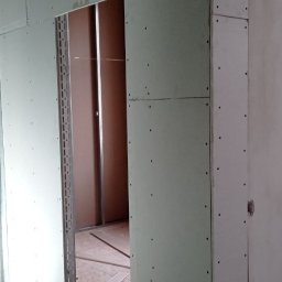 Vladyslav Vashchuk - Montaż płyt kartonowo-gipsowych wokół ościeżnicy drzwiowej, widoczne śruby i fragment instalacji elektrycznej w ścianie.