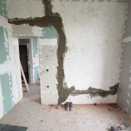 Vladyslav Vashchuk - Wnętrze w trakcie prac: ściany z płyt karton-gips, z widocznymi śladami szpachlowania i wzmocnieniami siatką, na podłodze robocze buty i narzędzia.