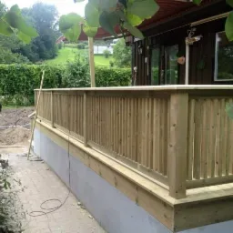 Nowy drewniany taras w trakcie budowy, widoczne niedokończone podłoże i ułożona częściowo kostka brukowa.