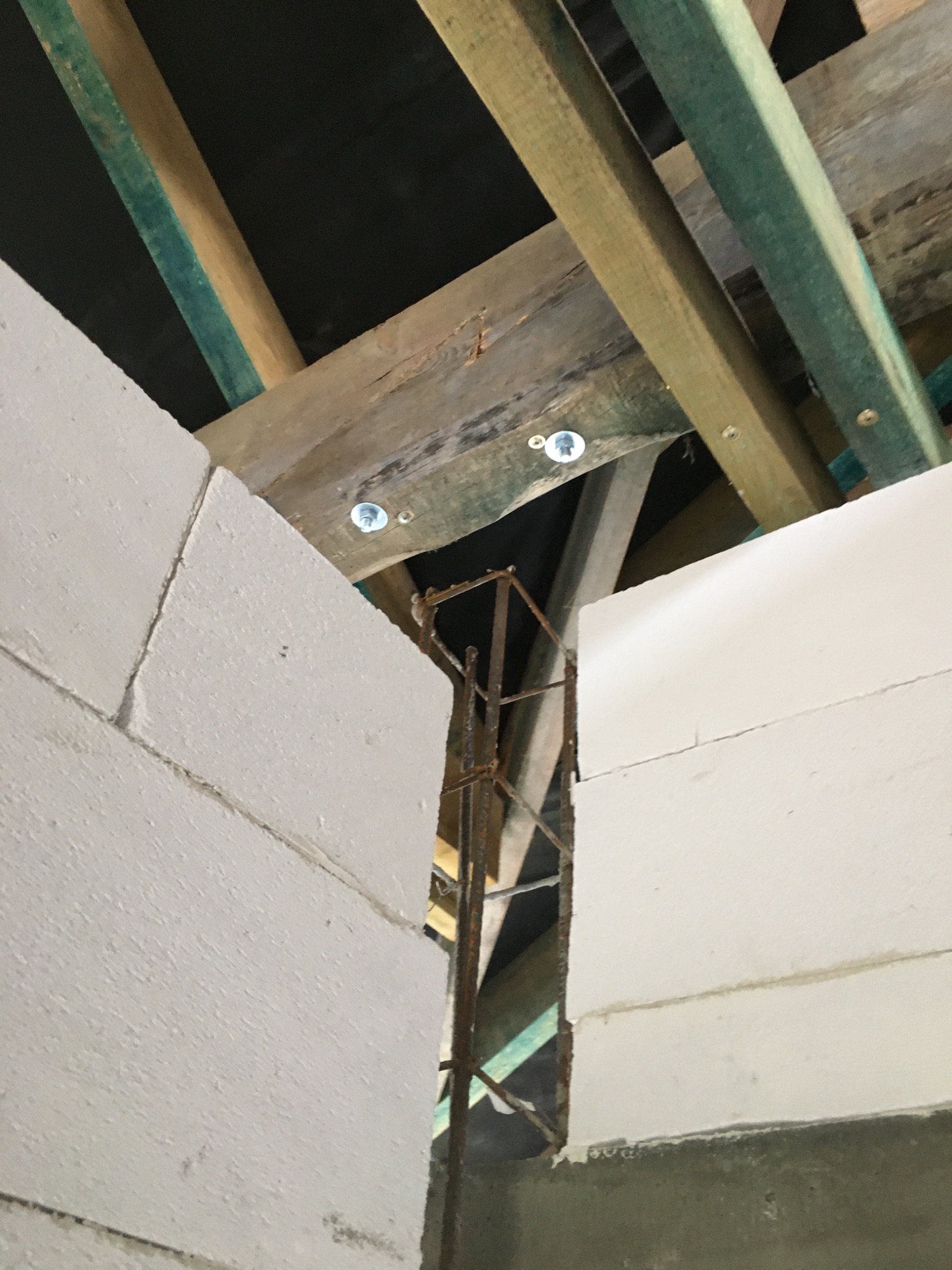 Wznoszenie ściany z bloczków betonu komórkowego Ytong, widoczne zbrojenie pionowe i elementy konstrukcji dachu z drewnianymi belkami mocowanymi na śruby.