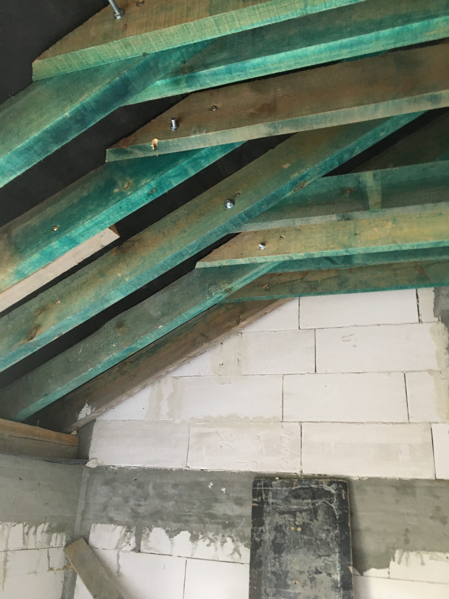 Wnętrze w trakcie budowy: ściana z białych bloczków, zielone drewniane belki stropowe mocowane śrubami, fragment betonowej wylewki.