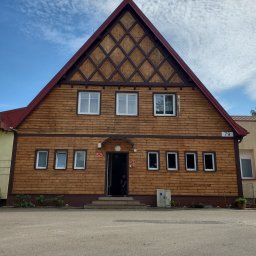 Firma Handlowo Usługowa Łukasz Jarząbek - Drewniana elewacja budynku z numerem 79, z widocznym wzorem kratownicy pod dachem i kilkoma oknami, na tle błękitnego nieba z obłokami.