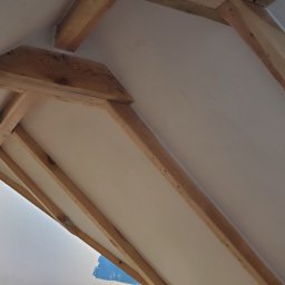 Firma Handlowo Usługowa Łukasz Jarząbek - Skośny sufit poddasza z drewnianą konstrukcją nośną, częściowo pomalowany na biało, widoczne fragmenty niepomalowanej ściany.