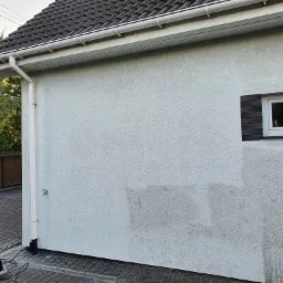 Fragment elewacji budynku z widocznymi śladami po czyszczeniu, z myjką ciśnieniową na pierwszym planie.