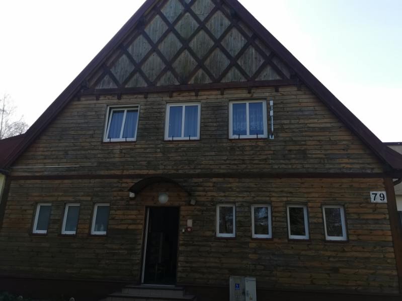 Dwupiętrowy dom z drewnianą elewacją i dachem w kształcie litery A, z widocznym numerem '79' na ścianie.