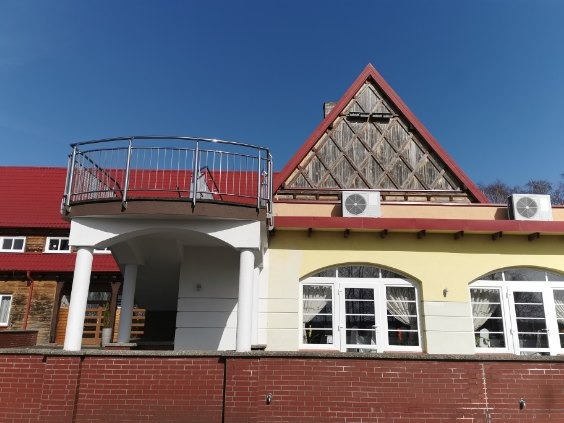 Budynek z czerwonym dachem, balkonem z metalową balustradą, oknami łukowymi i drewnianym szczytem z dwoma klimatyzatorami.