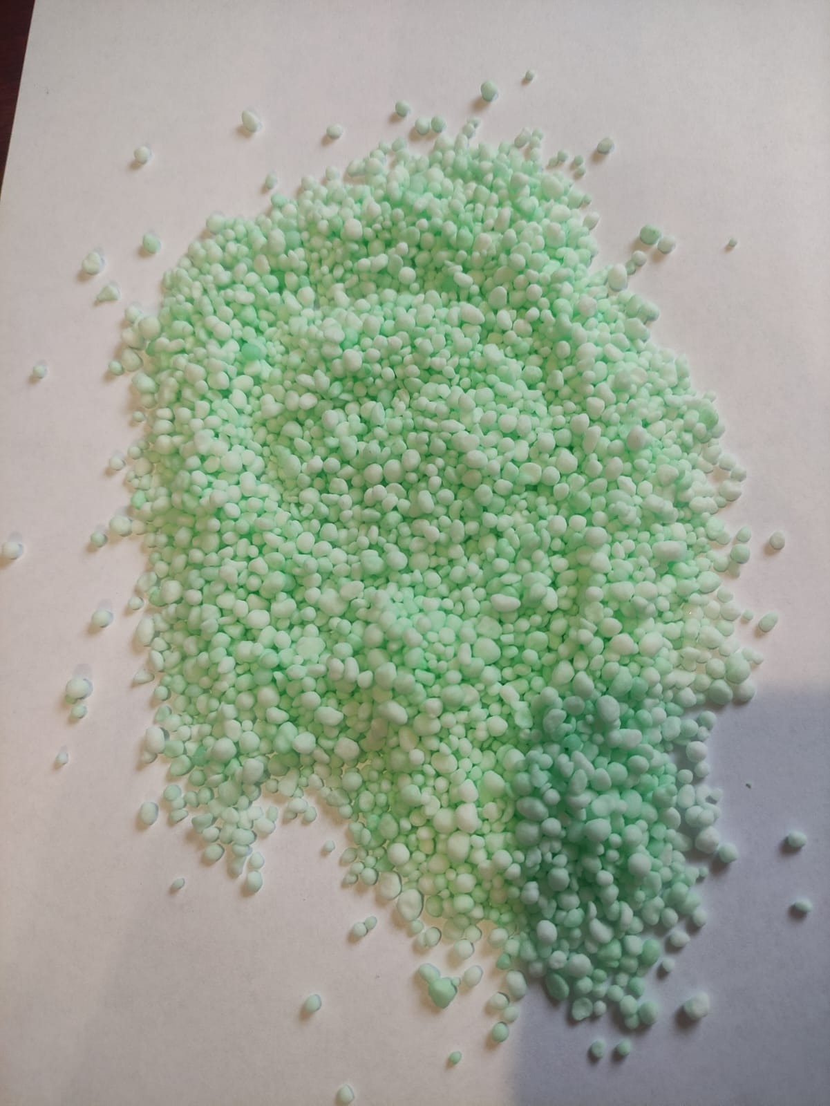 Jasnozielone granulki nawozu rozsypane na białym tle, widoczne pojedyncze grudki.