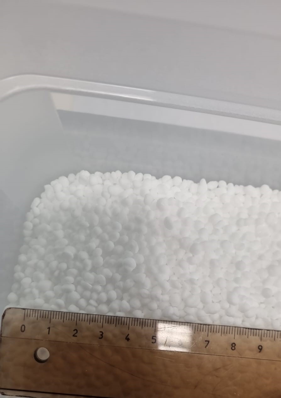 Białe granulki w przezroczystym pojemniku, zmierzone linijką.