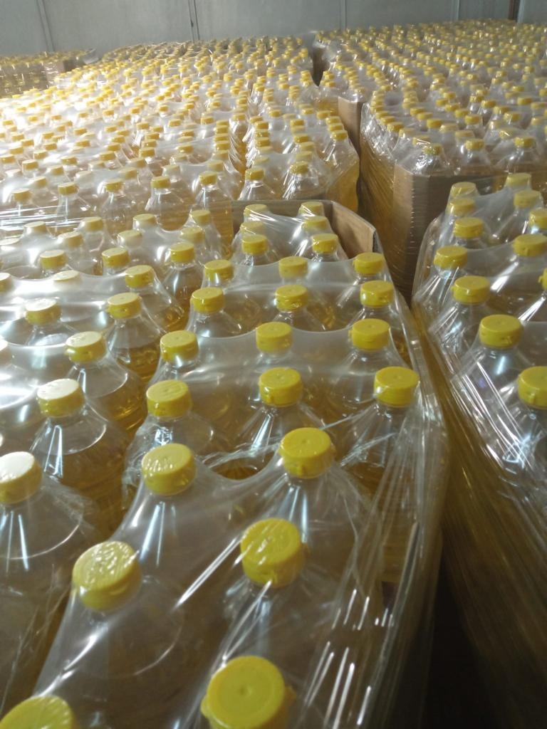 Magazyn pełen palet z butelkami przezroczystego oleju z żółtymi zakrętkami, zapakowanymi w folię termokurczliwą.