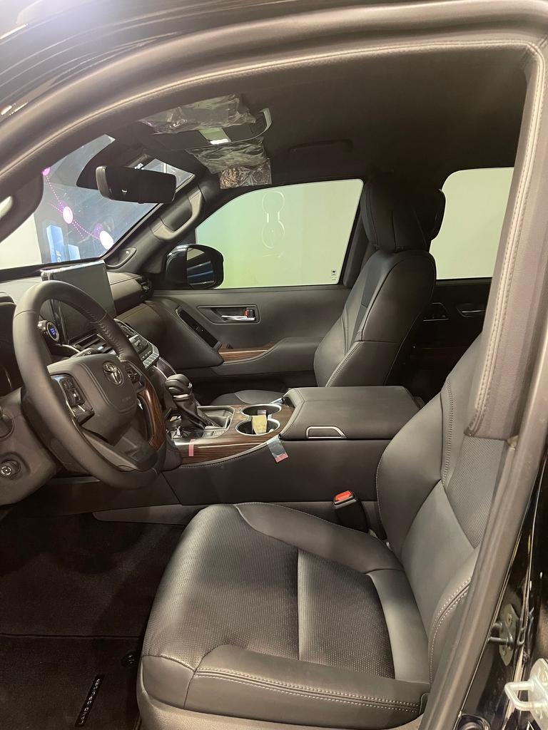 Wnętrze luksusowego samochodu, widok z boku na skórzane fotele, deskę rozdzielczą z elementami drewnianymi oraz kierownicę, z widocznym logo producenta na kierownicy.