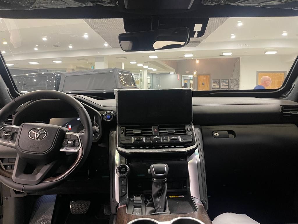 Wnętrze nowego samochodu Toyota z widoczną deską rozdzielczą, kierownicą i centralnym panelem sterowania, z salonem samochodowym widocznym w tle.