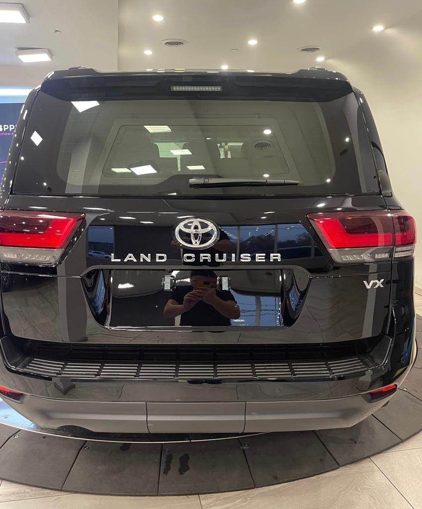 Tył czarnego samochodu Land Cruiser VX z widocznym logo i napisem, z odbiciem osoby robiącej zdjęcie w karoserii.