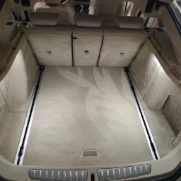 Wnętrze bagażnika samochodu osobowego z jasną, tekstylną wyściółką podłogi, widoczne szyny mocujące i oświetlenie LED.