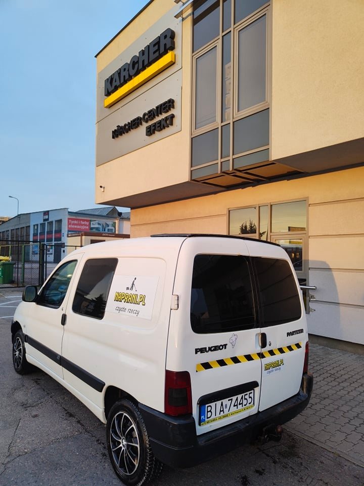 Biały samochód dostawczy Peugeot Partner z naklejką firmy sprzątającej 'NAPRAMI.PL czyste rzeczy' zaparkowany przed budynkiem Kärcher Center Efekt w słoneczny dzień.