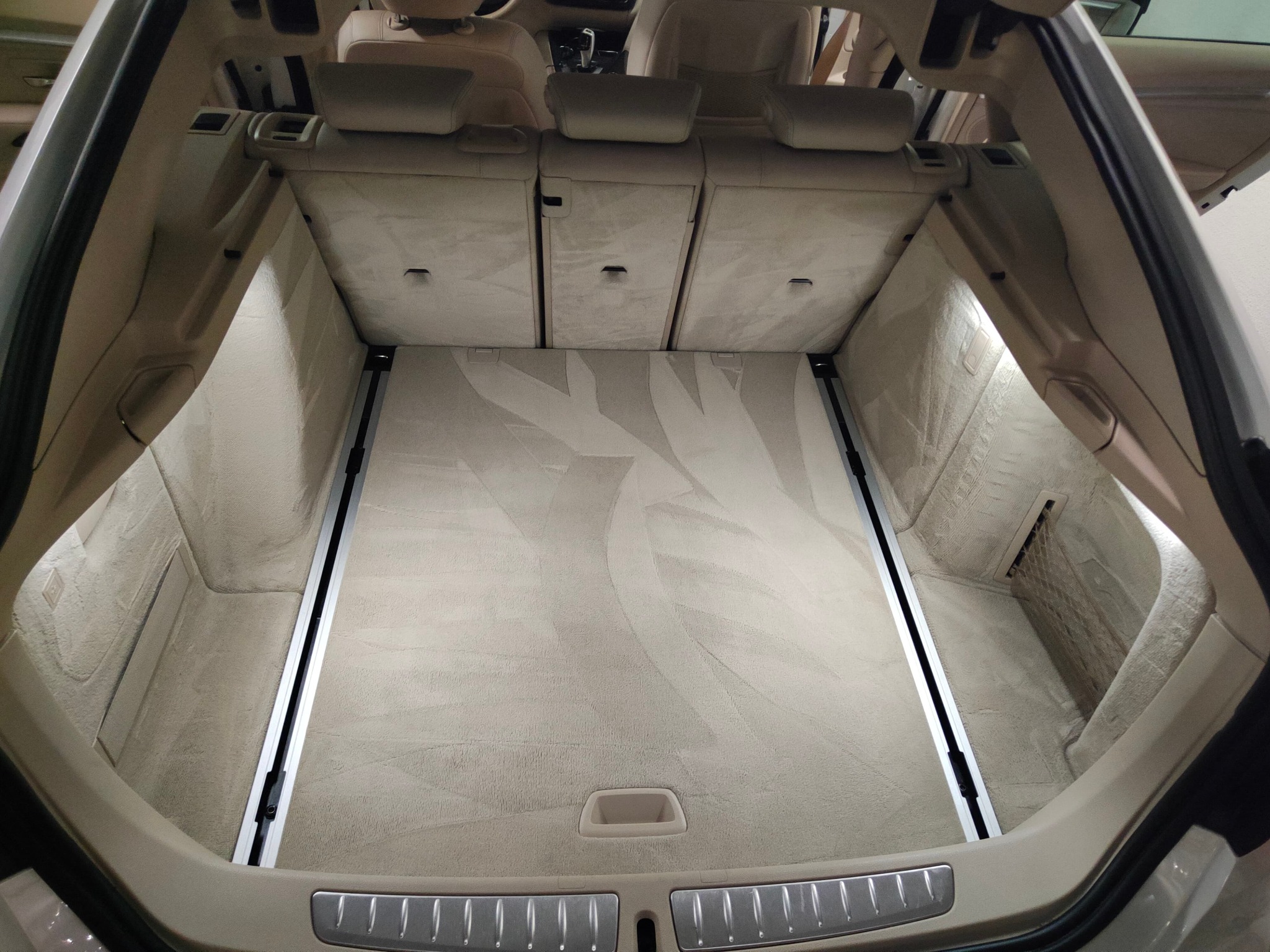 Wnętrze bagażnika samochodu osobowego z jasną, tekstylną wyściółką podłogi, widoczne szyny mocujące i oświetlenie LED.