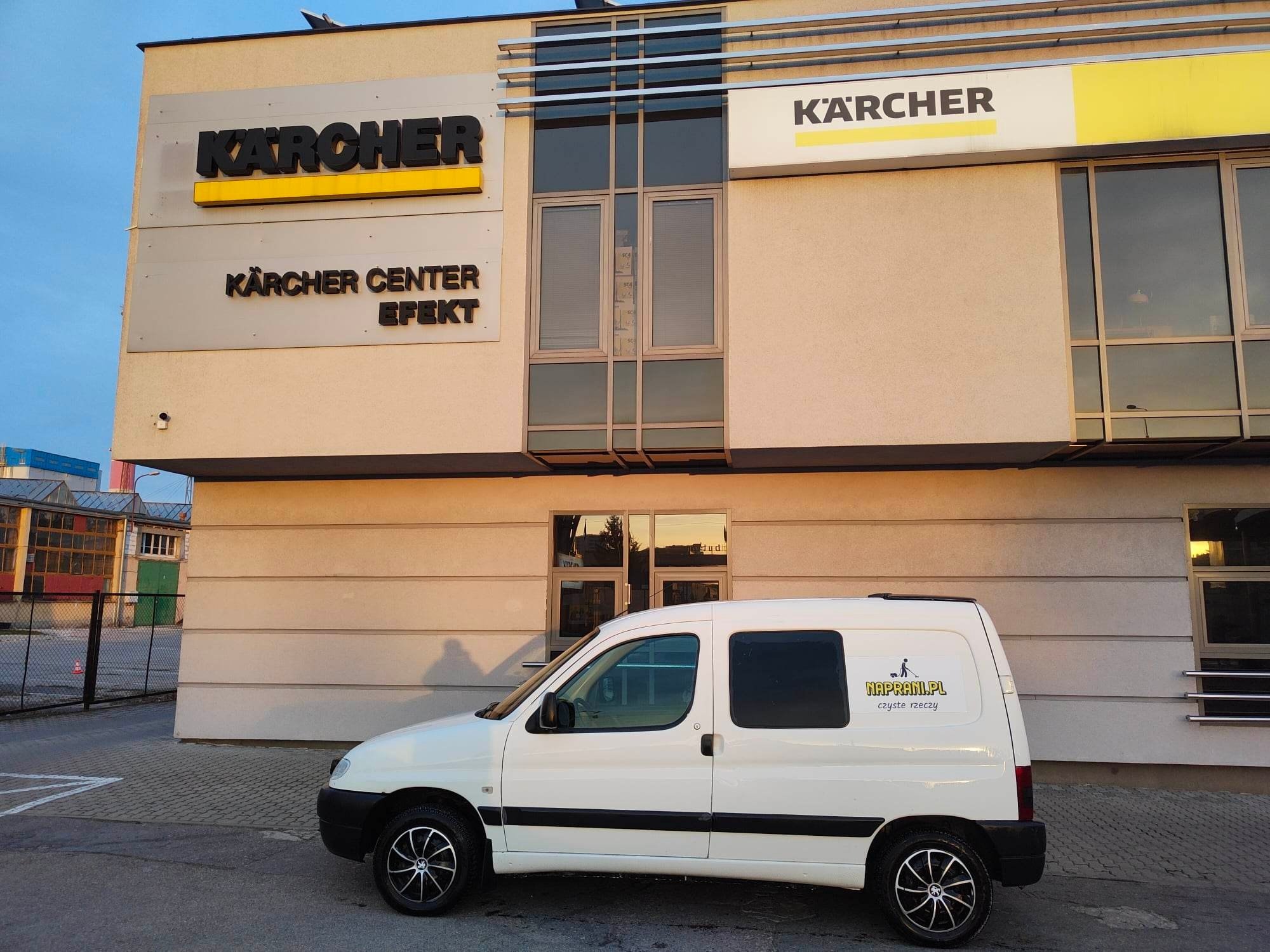 Biały samochód dostawczy z logo 'naprani.pl czyste rzeczy' zaparkowany przed budynkiem Kärcher Center Efekt w słoneczny dzień.