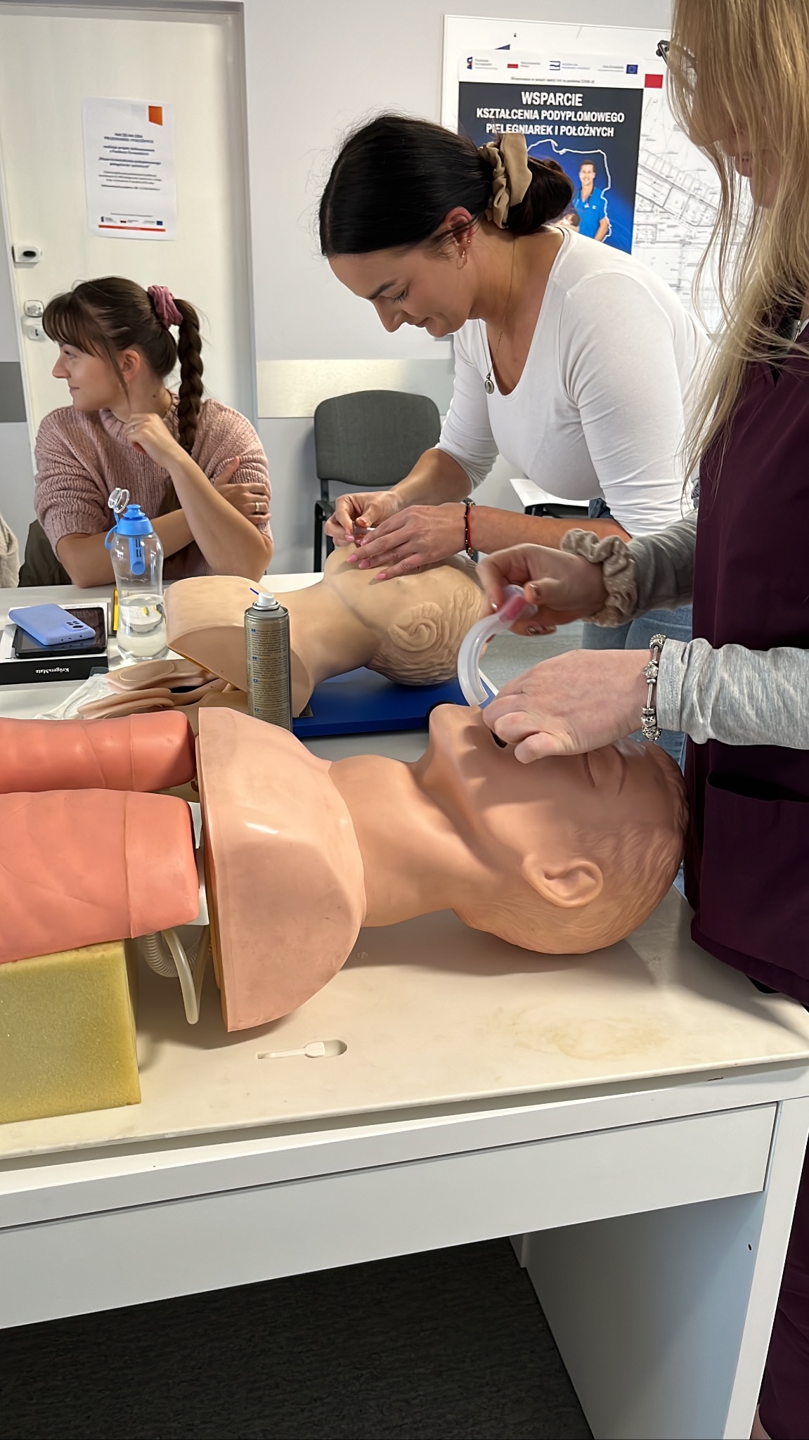 Instruktorzy demonstrujący techniki resuscytacji na manekinach podczas szkolenia, widoczne narzędzia i materiały szkoleniowe.