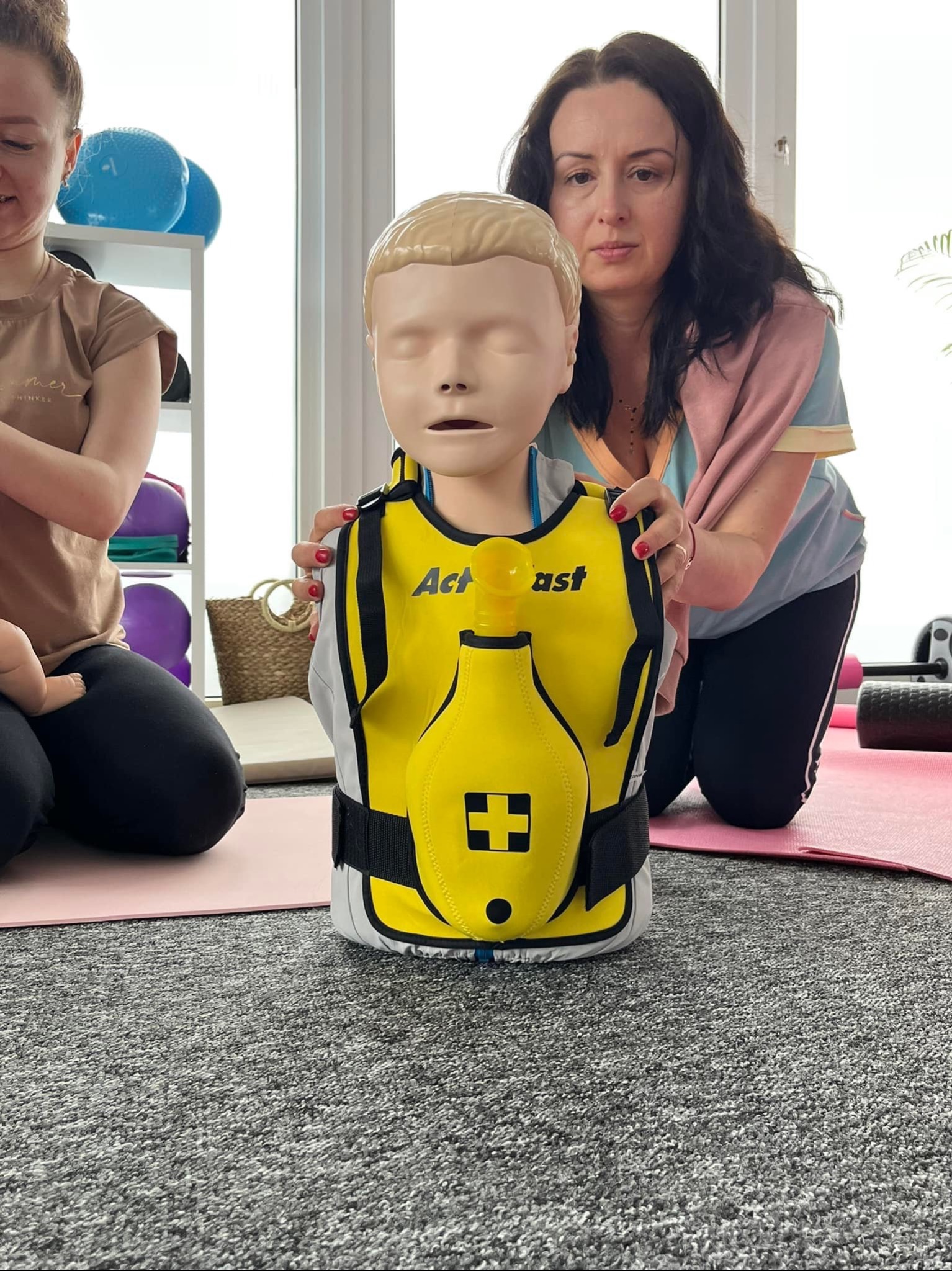 Instruktor z Rostarzewa demonstruje na manekinie resuscytację krążeniowo-oddechową podczas szkolenia z pierwszej pomocy, widoczna kamizelka z symbolem krzyża.