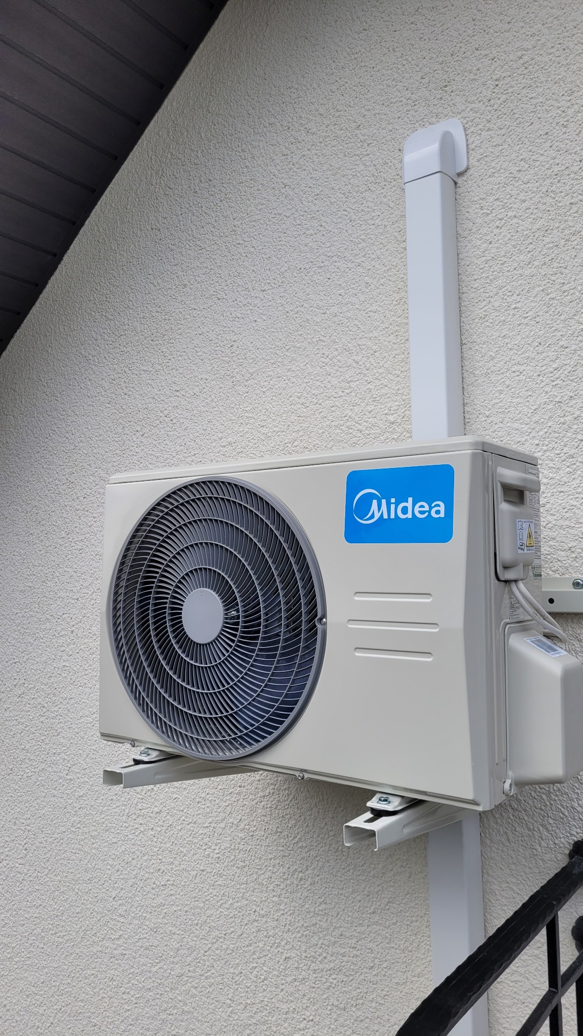 Zewnętrzna jednostka klimatyzacji Midea Blanc Pro 2.6kW zamontowana na elewacji budynku z widoczną instalacją odprowadzającą skropliny.