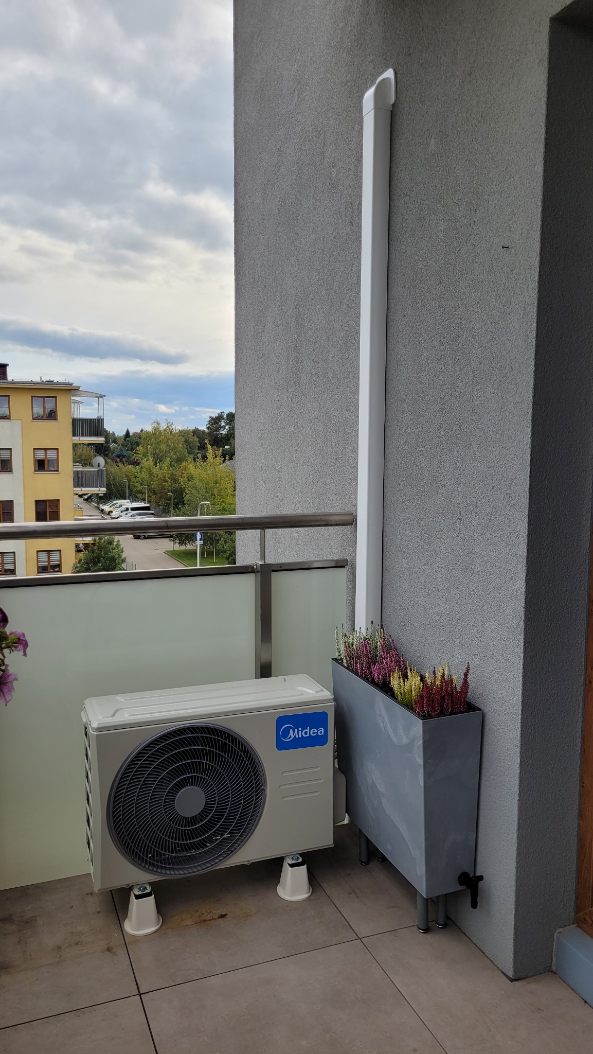Jednostka zewnętrzna klimatyzacji Midea Blanc Pro 3.5kW zamontowana na balkonie, widoczny odpływ skroplin i donica z wrzosami.
