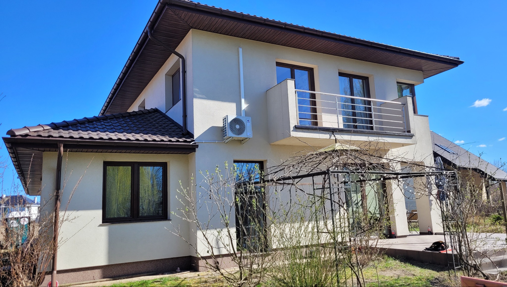 Biały budynek jednorodzinny z zamontowanym klimatyzatorem Gree Pular 3.2kW na ścianie, widok z zewnątrz w słoneczny dzień.