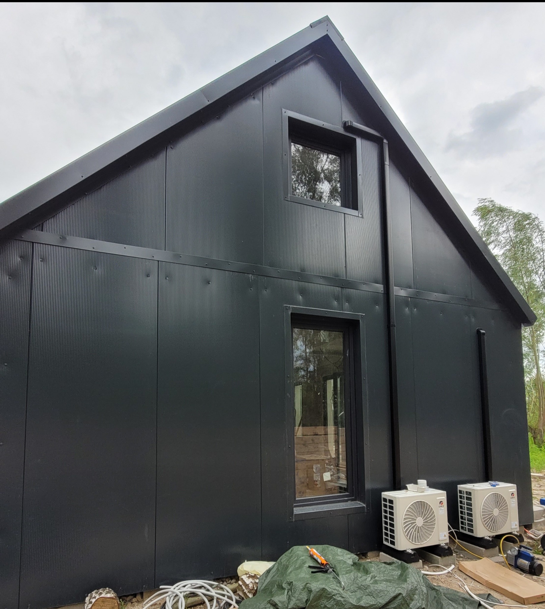 Elewacja domu z dwoma zamontowanymi klimatyzatorami Gree Pular. Widoczna instalacja odprowadzająca skropliny. Na ziemi narzędzia i materiały montażowe.