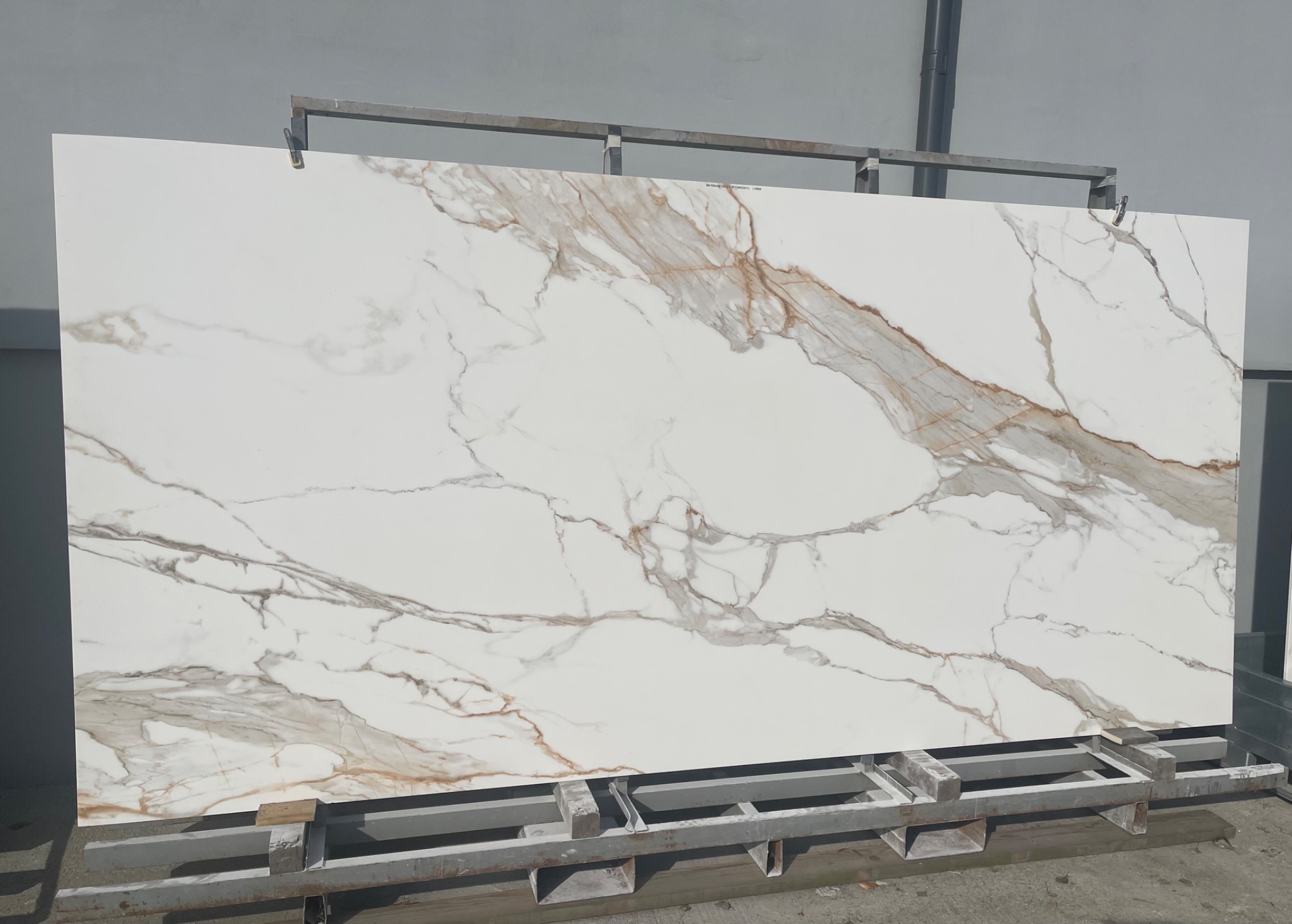 Duża płyta z białego materiału z brązowymi żyłami, oparta na metalowym stojaku.