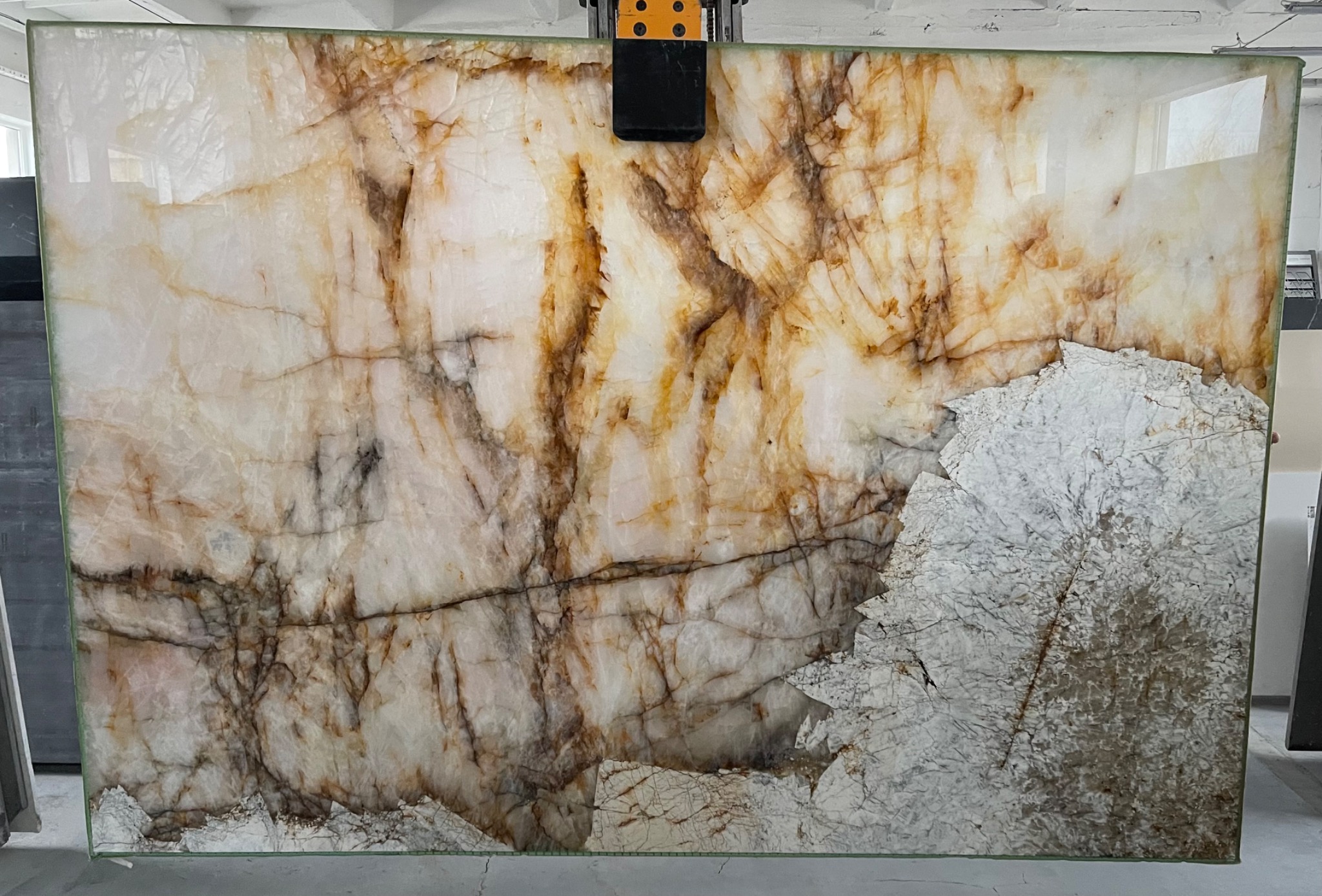 Duża płyta z onyksu w odcieniach bieli i brązu, zabezpieczona na czas transportu, widoczne naturalne spękania i żyły kamienia.