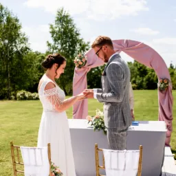 Para wymienia się obrączkami podczas ceremonii ślubnej na świeżym powietrzu, z łukiem dekoracyjnym i kwiatami.