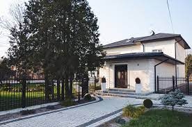 Nowoczesny dom jednorodzinny z jasną elewacją, ciemnym dachem i zadbanym ogrodem z podjazdem wyłożonym kostką brukową.