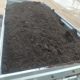 Przyczepa marki Martz Premium wypełniona ziemią ogrodową, widok z góry na brudną, mokrą nawierzchnię placu.