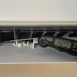 JAKU Jakub Wójcik - Pomiar temperatury klimatyzatora za pomocą termometru cyfrowego REFCO, wskazującego 42.0°C, podczas serwisu. Widoczny fragment dłoni.