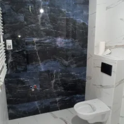 Wykończona łazienka z ciemnymi płytkami imitującymi marmur na ścianie, białą ceramiką sanitarną i grzejnikiem drabinkowym po lewej stronie.