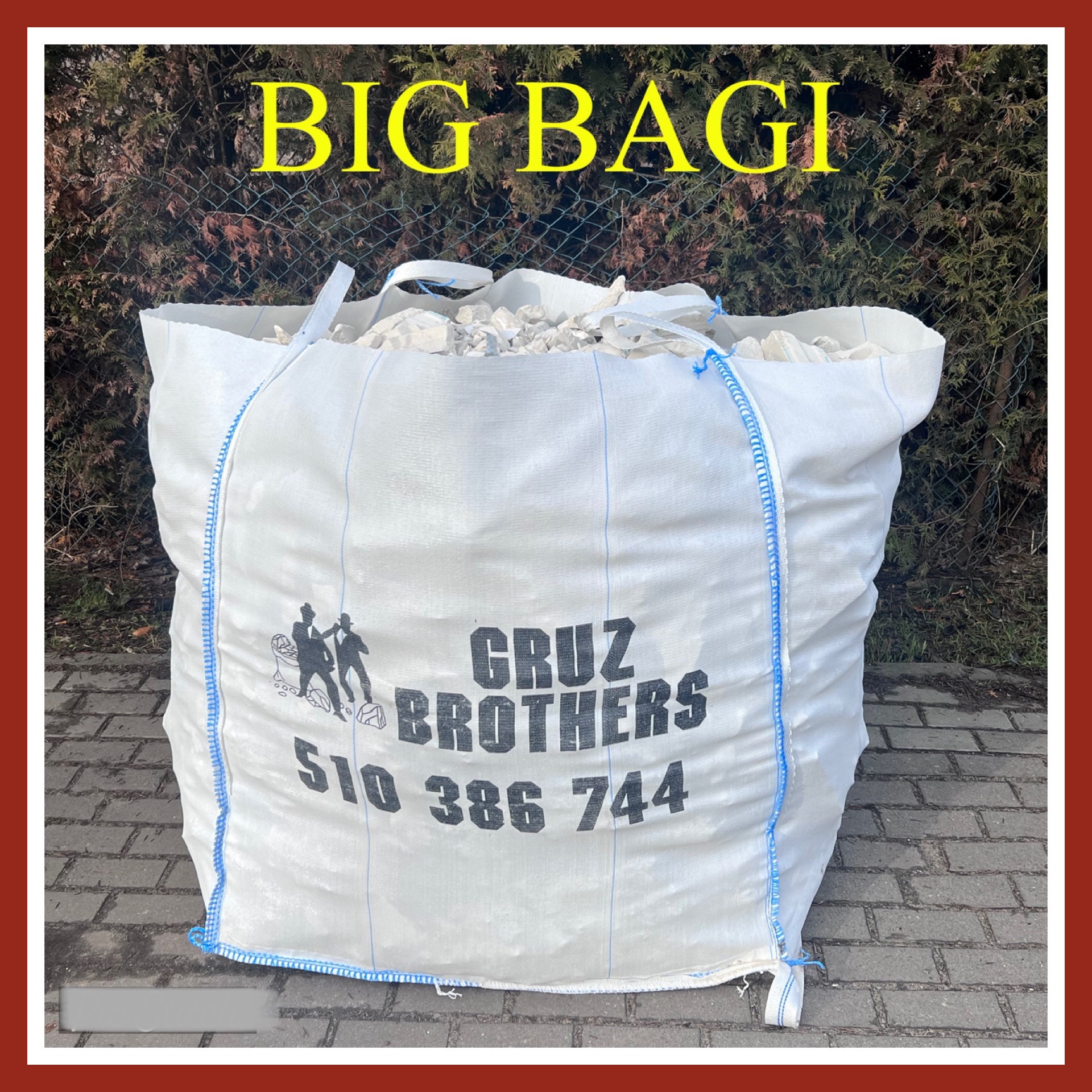 Duży, biały worek typu Big Bag wypełniony białym gruzem, z nadrukiem nazwy firmy 'Cruz Brothers' i numerem telefonu, stojący na brukowanej powierzchni z zielonymi krzewami w tle.