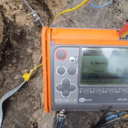 Miernik Sonel MPI-530 podczas pomiaru rezystancji uziemienia w wykopie, widoczna sonda wbita w ziemię i przewody pomiarowe.