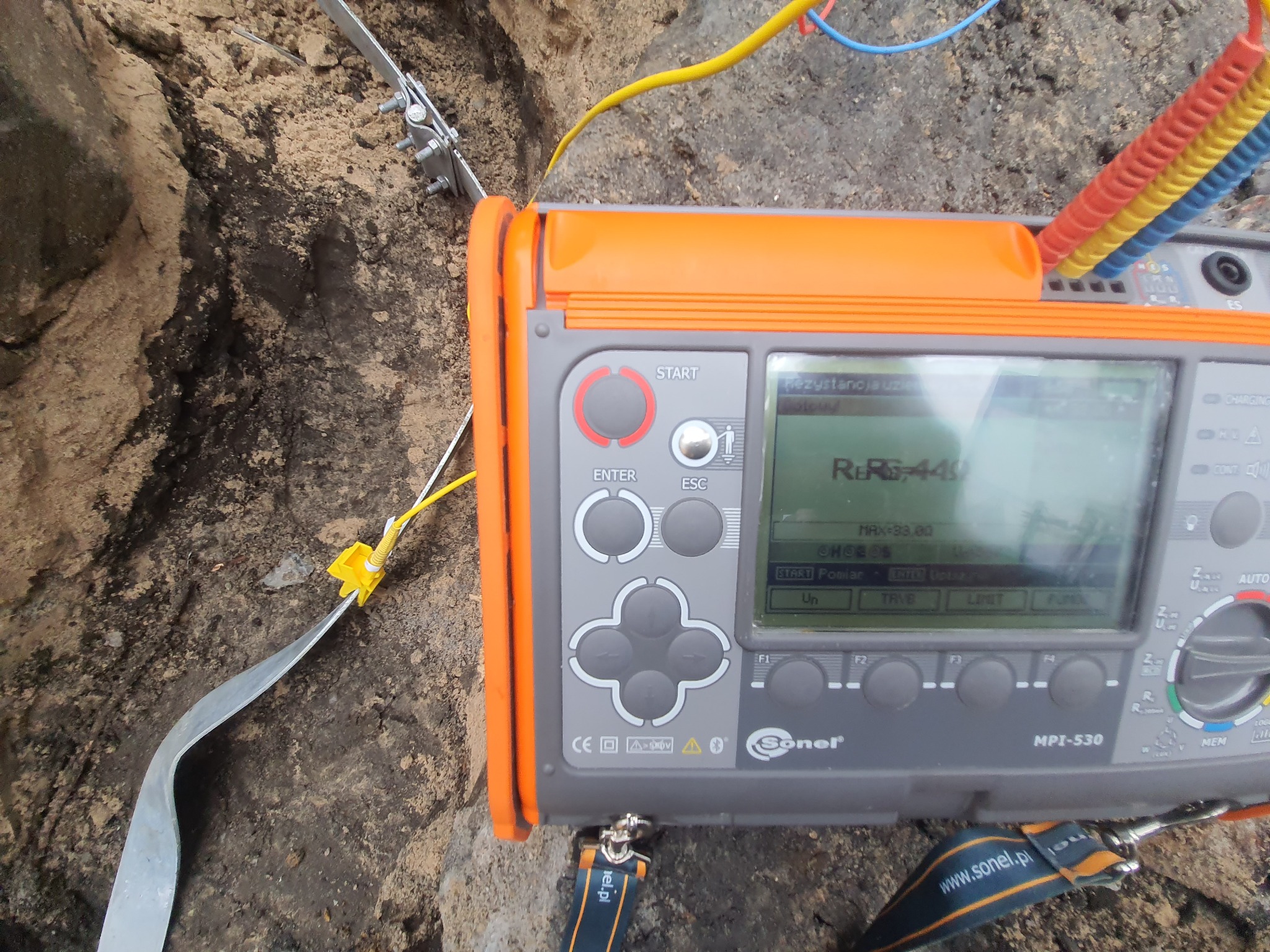 Miernik Sonel MPI-530 podczas pomiaru rezystancji uziemienia w wykopie, widoczna sonda wbita w ziemię i przewody pomiarowe.