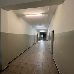 AD-REM FIRMA USŁUGOWA ADAM GRACZYK - Korytarz po odświeżeniu w Lniano: ściany pomalowane na dwa kolory, jasna góra i ciemniejszy dół. Brązowa podłoga z płytek, sufit z lampami. Widok w głąb korytarza.