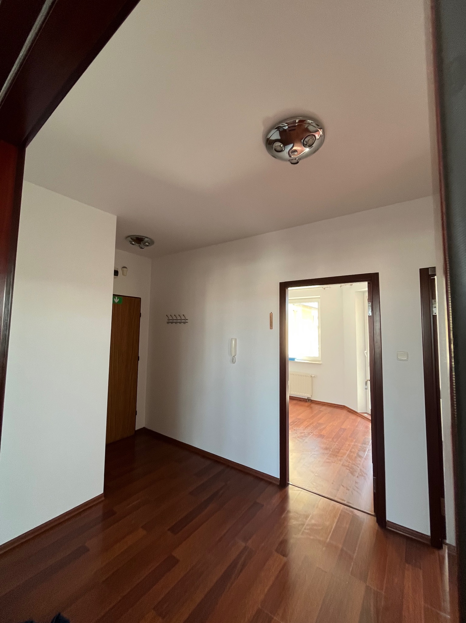 Korytarz po remoncie: świeżo pomalowane ściany w odcieniach bieli, ciemne drewniane panele podłogowe, widoczne drzwi wejściowe i przejście do innego pomieszczenia.