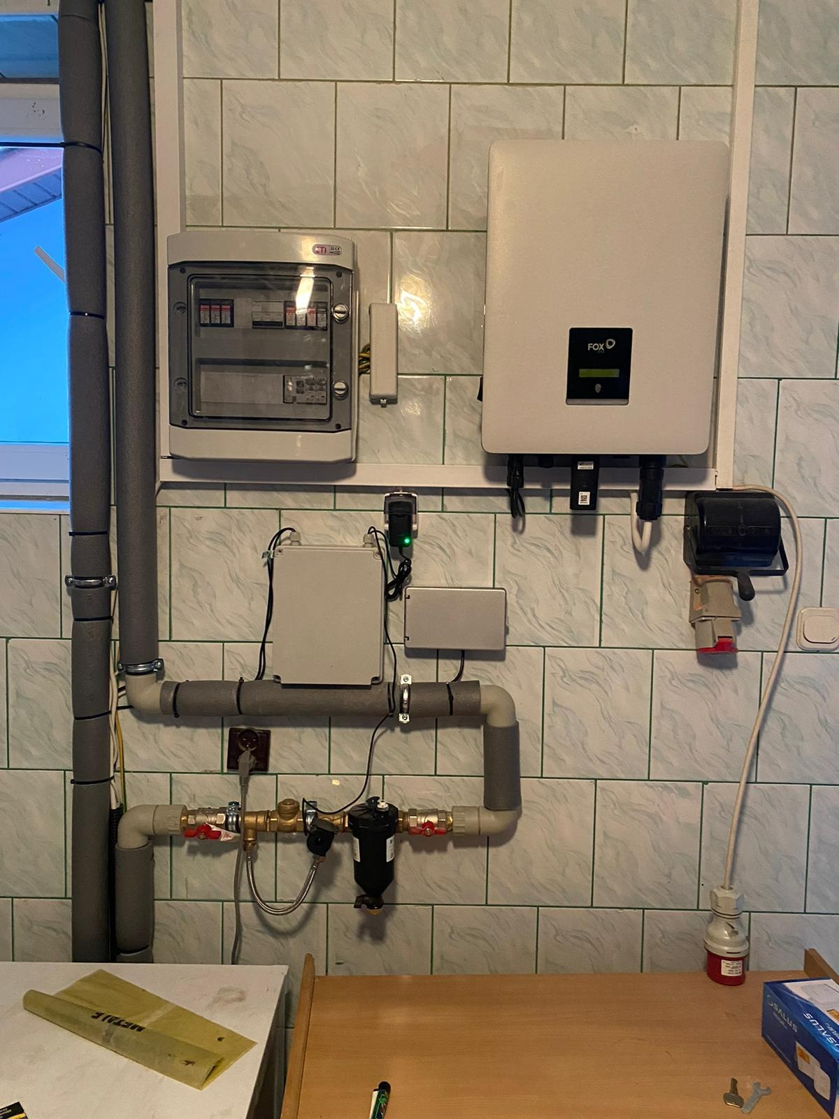 Instalacja wewnętrzna z rozdzielnicą elektryczną, inwerterem marki FOX, rurami izolowanymi termicznie, filtrem i zaworami, zamontowana na ścianie wyłożonej kafelkami.