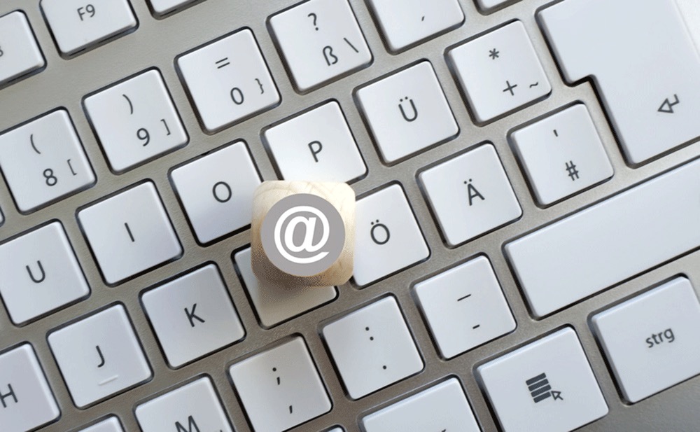 Klawiatura komputera z drewnianym sześcianem z symbolem @ na klawiszu 'P'.