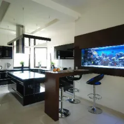 Nowoczesna kuchnia z czarnymi szafkami i wyspą, oświetlona wiszącymi lampami, zintegrowana z barkiem i dużym akwarium w zabudowie.