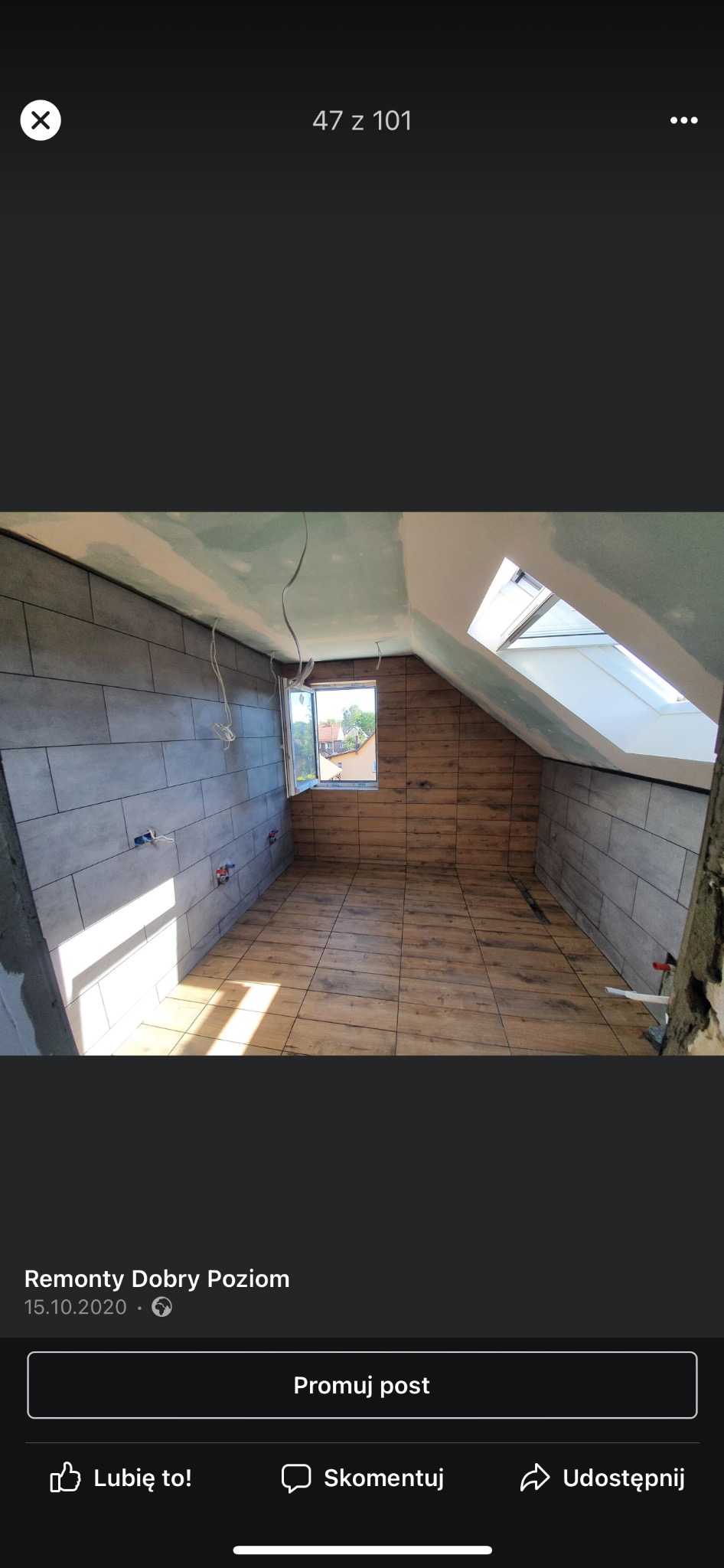 Poddasze w trakcie prac wykończeniowych: szare płytki imitujące kamień na ścianach do połowy wysokości, drewnopodobne płytki na podłodze, odsłonięte kable elektryczne, okno dachowe i okno w ścianie...