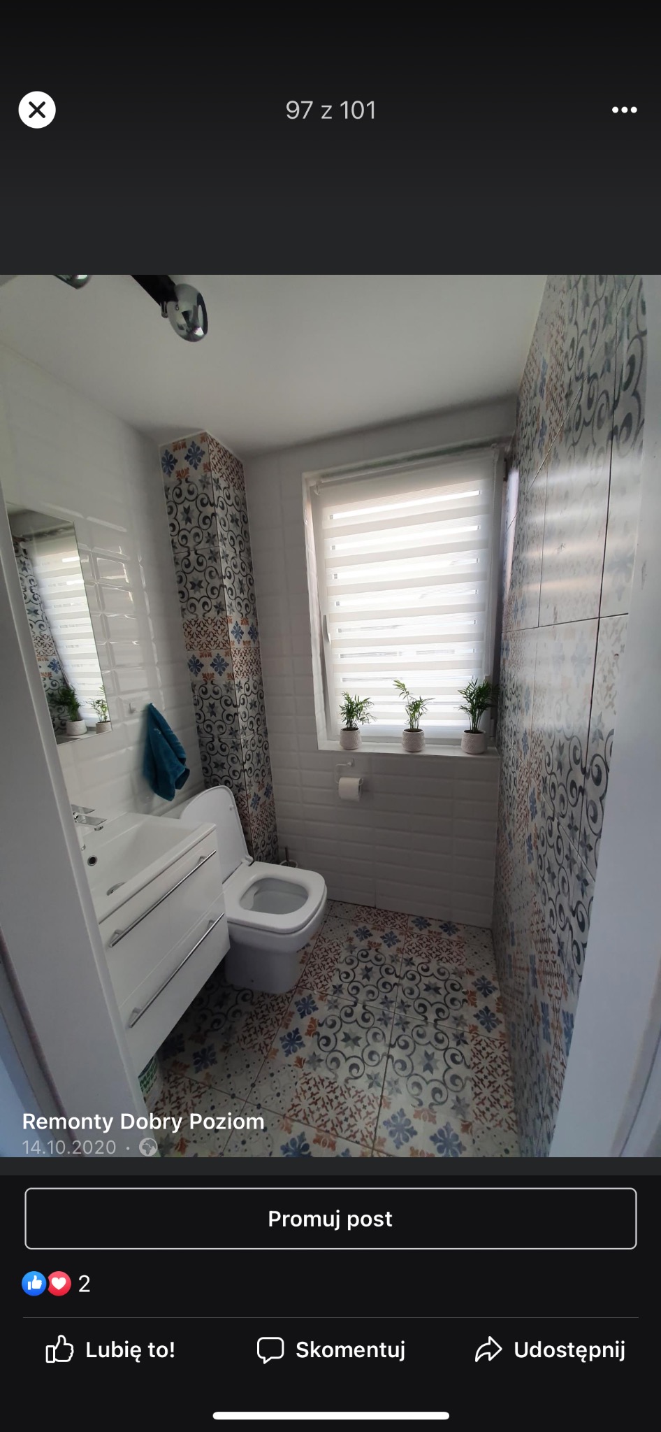 Wnętrze łazienki po remoncie: białe płytki imitujące cegłę, dekoracyjne płytki z motywem kwiatowym na ścianie i obudowie pionu, wzorzysta podłoga, biała umywalka z szafką, toaleta i rolety w oknie...